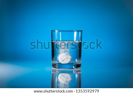 Effervescent tablet dissolving in a glass of water at blue background with copy space