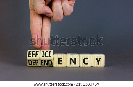 Efficiency or dependency symbol. Businessman turns cubes, changes the word dependency to efficiency. Beautiful grey table, grey background, copy space. Business, efficiency or dependency concept.