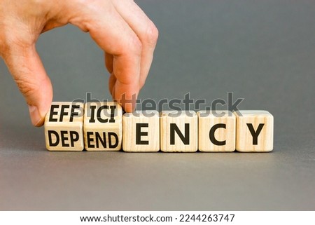 Efficiency or dependency symbol. Businessman turns cubes, changes the word dependency to efficiency. Beautiful grey table, grey background, copy space. Business, efficiency or dependency concept.