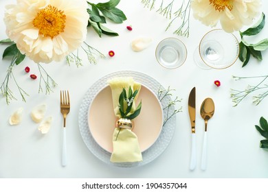 Effortless Golden Birthday Dinner Table Decor. Pale Yellow Peony Flowers And Late Spring, Summer Flat Lay. White Dinner Table, White And Gold Utensils, Decorated With Flowers And Greens.