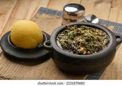 Efik Afang soup served in a clay bowl with garri on a wooden background - Shutterstock ID 2131870683