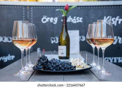 Eger, Hungary – October 17, 2022. Wine Tasting At The Valley Of The Beautiful Women In Eger, Hungary. Six Glasses Of Leanyka And Olaszrizling White And Rose Wines And A Cheese Plate With Grapes. 