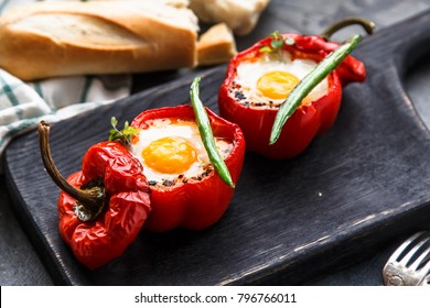 Egg baked in red bell pepper with sausage and tomato on a black board, close view