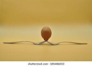 egg balanced on a composition of 2 intertwined forks isolated over neutral orange background