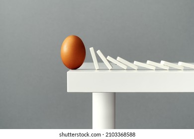 Egg balancing on the edge of a table, about to fall down and break due to domino tiles falling