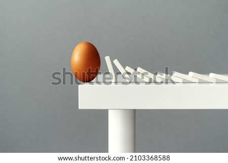 Egg balancing on the edge of a table, about to fall down and break due to domino tiles falling