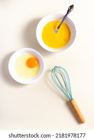 Egg Beat, Egg Shell With Whisk. Raw Eggs In A Glass And White Bowl On The Table. Flat Lay. Broken White Background. 