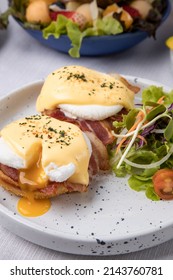 Egg Benedict - Toasted English Muffins, Ham, Poached Eggs, Smoked Bacon Avocado And Delicious Buttery Hollandaise Sauce With A Dish Of Fruit Salad