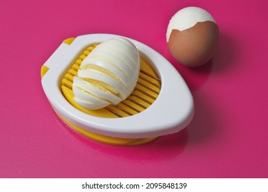 Egg Cutter On A Pink Background. Boiled Egg, Cut Open And Egg Partially Peeled.