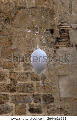 egg dancing on water column, creating a splash of drops on a background of rustic stone wall - Ou com balla