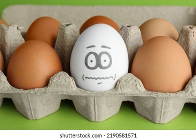 Egg With Drawn Frightened Face Among Others In Cardboard Package, Closeup