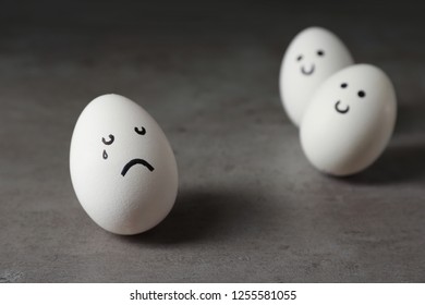 Egg with drawn sad face near happy ones on table. Threat of depression
