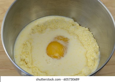 Egg And Evaporated Milk On Top Of Cornbread Mix In Stainless Steel Mixing Bowl