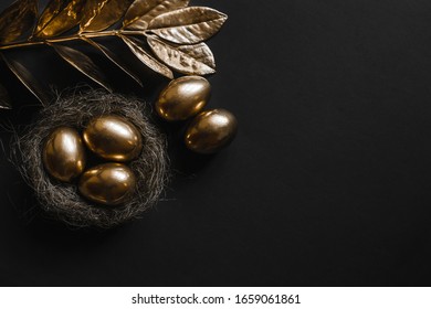 
The Egg Is Painted Gold In A Straw Nest And The Plant With Golden Leaves On A Black Background With A View From Above.A Background For Celebrating Easter. Top View,Flatlay.