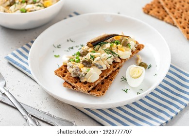 Egg salad with anchovies on crispy bread. Sandwich with Swedish egg salad gubbröra in a plate on a white concrete background close-up. Scandinavian cuisine.