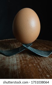 Egg set on rusty fork with wooden cutting board in dark environment