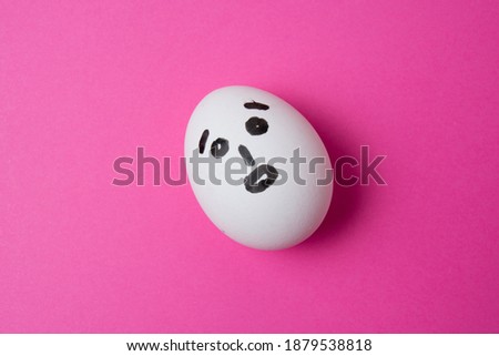 Egg with a surprised face on pink background with copy space.