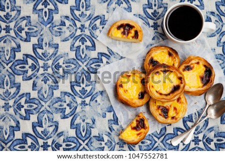 Egg tart, traditional Portuguese dessert, pastel de nata on a parchment paper. Blue textile background. Top view. Copy space.