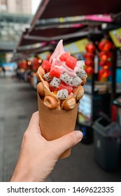 Egg Waffle Cone With Fruits In Hand. Pitahaya And Watermelon Pieces Combined With Strawberry Ice Cream.