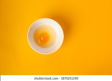  Egg With Yolk In A Bowl On A Yellow Background. Minimalist Concept Of Cooking