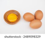 The egg yolk is in a wooden cup on a white background. It is the yolk of a chicken egg. It looks delicious and healthy.