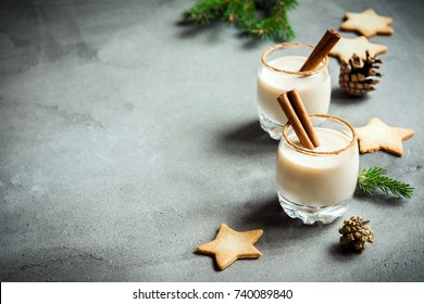 Eggnog with cinnamon and nutmeg for Christmas and winter holidays. Grey concrete background with Christmas Eggnog, gingerbread cookies, pine cones, copy space. - Powered by Shutterstock