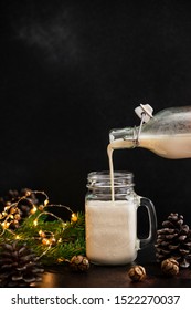 Eggnog Traditional Christmas Alcoholic Drink With Cinnamon And Nutmeg. Eggnog Pouring From A Bottle Into A Jar. Winter Holidays Mood. Dark Background. 