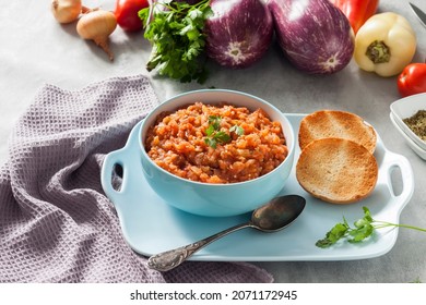 Eggplant caviar in blue bowl and fresh vegetables on background.