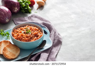 Eggplant caviar in blue bowl and fresh vegetables on background. Copy space