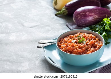 Eggplant caviar in blue bowl and fresh vegetables on background. Copy space