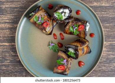 Eggplant rolls filled with goat cheese and decorated with green parsley and flowers, close up. Top view