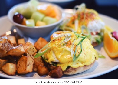 Eggs Benedict Breakfast With Fried Potatoes And A Fruit Salad