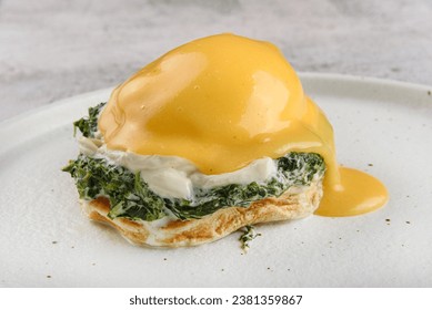 Eggs benedict or eggs florentine on a white plate. Eggs Benedict- toasted English muffins, poached eggs, spinach and delicious buttery hollandaise sauce.