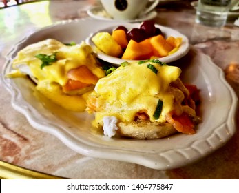 Eggs Benedict with side fruit in white plate on marble table