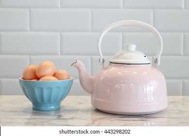 Eggs In Blue Bowl And Pink And White Stovetop Whistling Kettle On Table In The Kitchen.