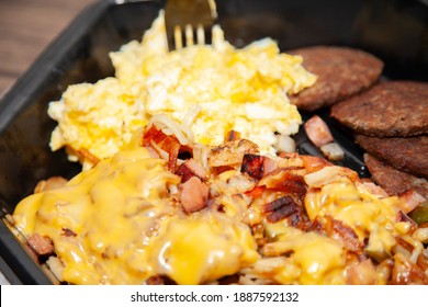 Eggs, Breakfast Sausage, And Cheesy Hash Browns In A Black Take Out Container