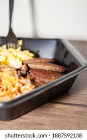 Eggs, Breakfast Sausage, And Cheesy Hash Browns In A Black Take Out Container