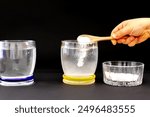 Eggs floating in saltwater experiment. Third step in black background. Two glasses full of water, and a transparent ramekin full of salt. A kid