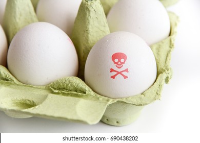 Eggs In A Green Paper Package With One Of The Eggs Painted With A Red Poisonous Risk Symbol Skull And Bones. Image Concept For Insecticide And Salmonella Egg Food Contamination.