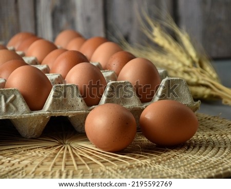 Eggs in a paper tray Placed on wicker and concrete floors. Garnish with dried barley. There is a background of blurry wooden planks.