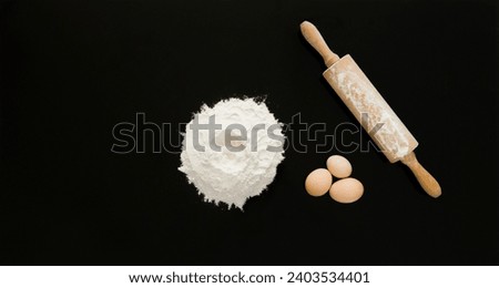 Eggs, rolling pin and flour on black background; top view