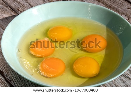 Eggs without shell. Broken chicken eggs in bowl of pale turquoise color, 5 pieces. Topic: benefits and harms of eating chicken eggs, cholesterol, cooking recipes, healthy natural products. 