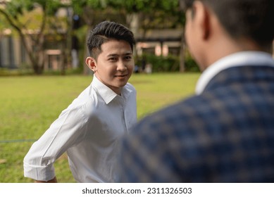 An egotistical and brash young asian man looking at another man cockily. Rivals or enemies in the workplace. - Shutterstock ID 2311326503