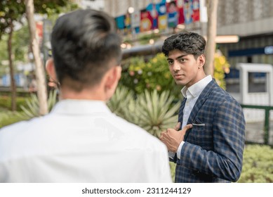 An egotistical young indian points to himself, bragging about his accomplishments to his colleague. Outdoor scene at the city business district. - Shutterstock ID 2311244129