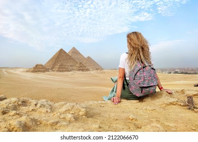 Egypt. Cairo - Giza. young blonde tourist girl with a backpack is sitting on the sand looking at General view of pyramids from the Giza Plateau. enjoy the beautiful view and relax. concept of tourism.