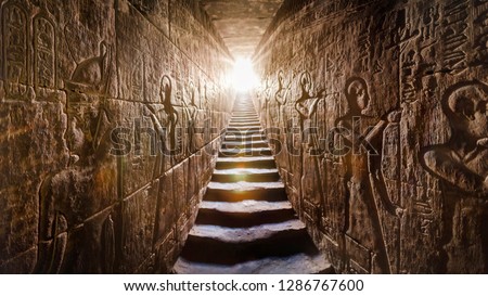 Egypt Edfu temple, Aswan. Passage flanked by two glowing walls full of Egyptian hieroglyphs, illuminated by a warm orange backlight from a door