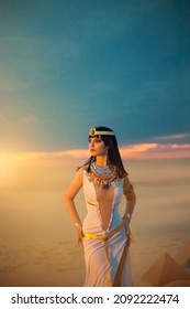 Egypt Style Rich Luxury Woman. Sexy Beautiful Girl Goddess Queen Cleopatra Stands, Yellow Sand Desert Pyramids. Art Ancient Pharaoh Costume White Dress Gold Accessories. Black Hair Wig Egyptian Makeup