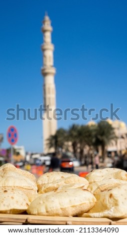 Egyptian bread Aish Baladi. A lot of fresh bread lies on the counter of a street cafe against the mosque minaret