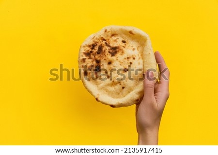 Egyptian bread Aish Baladi. Womans hand holding Fresh bread over yellow background