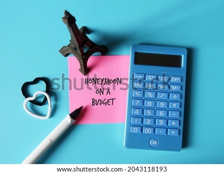Eiffel model,calculator,pen, two hearts on blue background, pink note written HONEYMOON ON A BUDGET, concept of planning cost for trip of a lifetime, newly wed couples calculate honeymoon trip cost